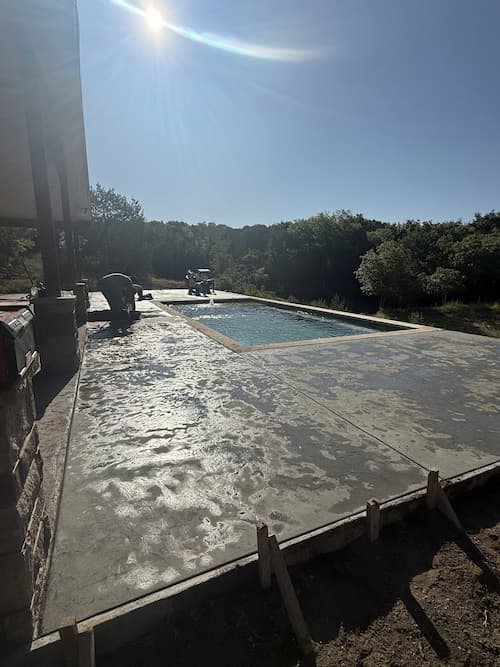 Crew pouring and finishing stamped concrete decking beside the pool