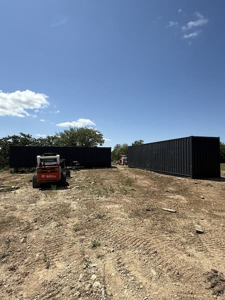 Two shipping containers set on cleared ground with equipment on site