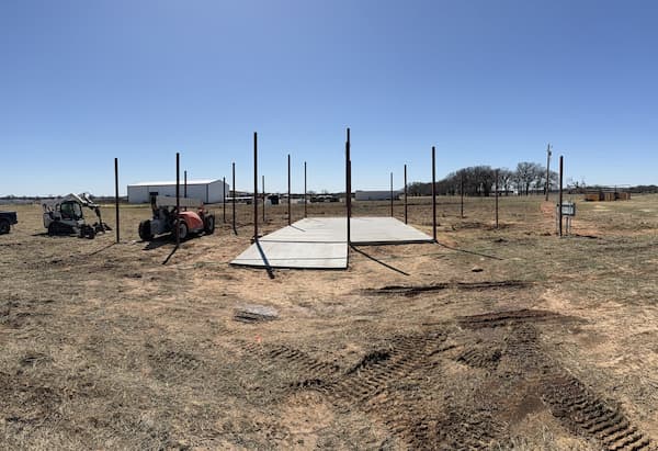 Steel posts standing in open pasture beside a freshly poured slab