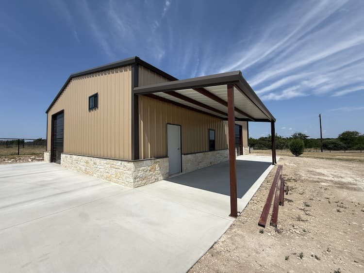 Finished tan metal shop with stone wainscot, roll up doors, and covered patio
